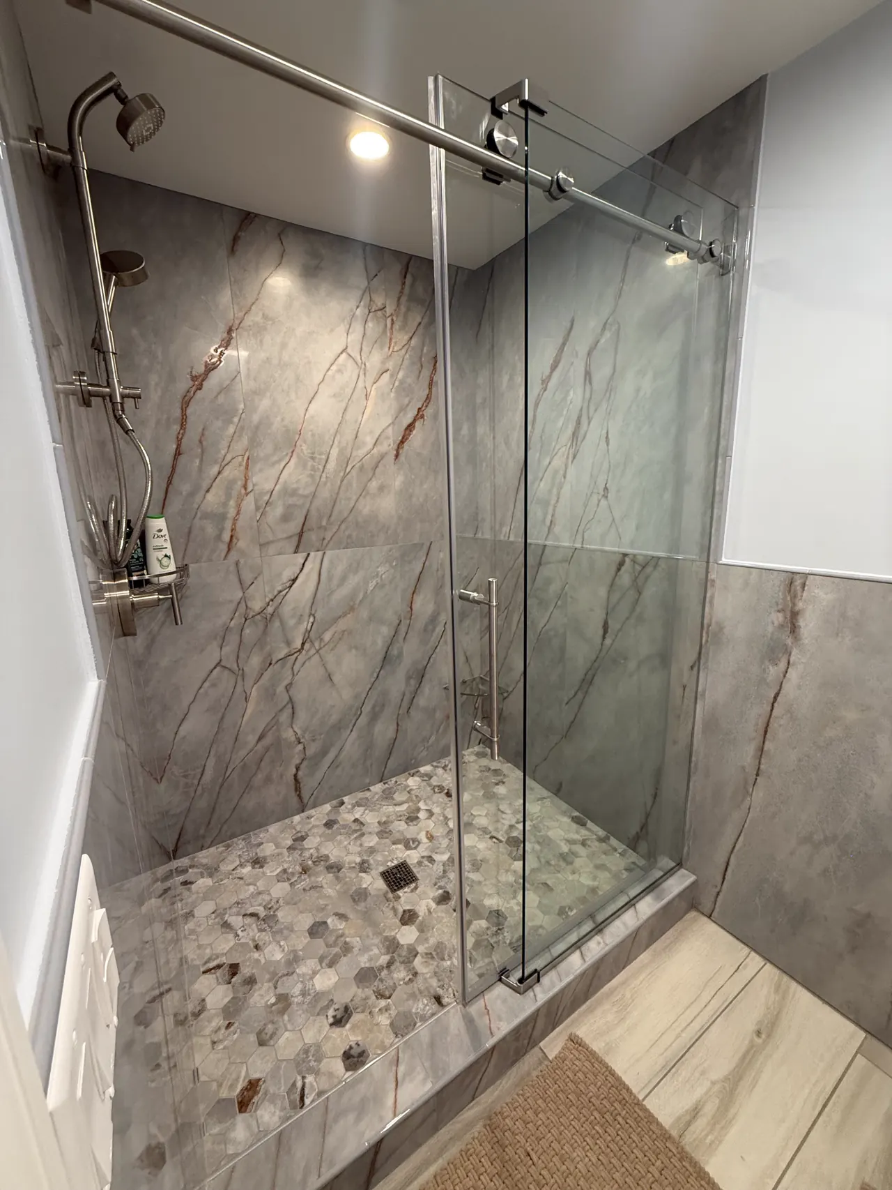 Walk-in shower with marble-look porcelain walls, a hex mosaic floor and a sliding glass door