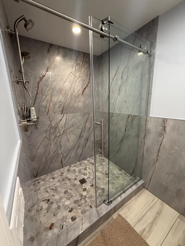 Walk-in shower with marble-look porcelain walls, a hex mosaic floor and a sliding glass door