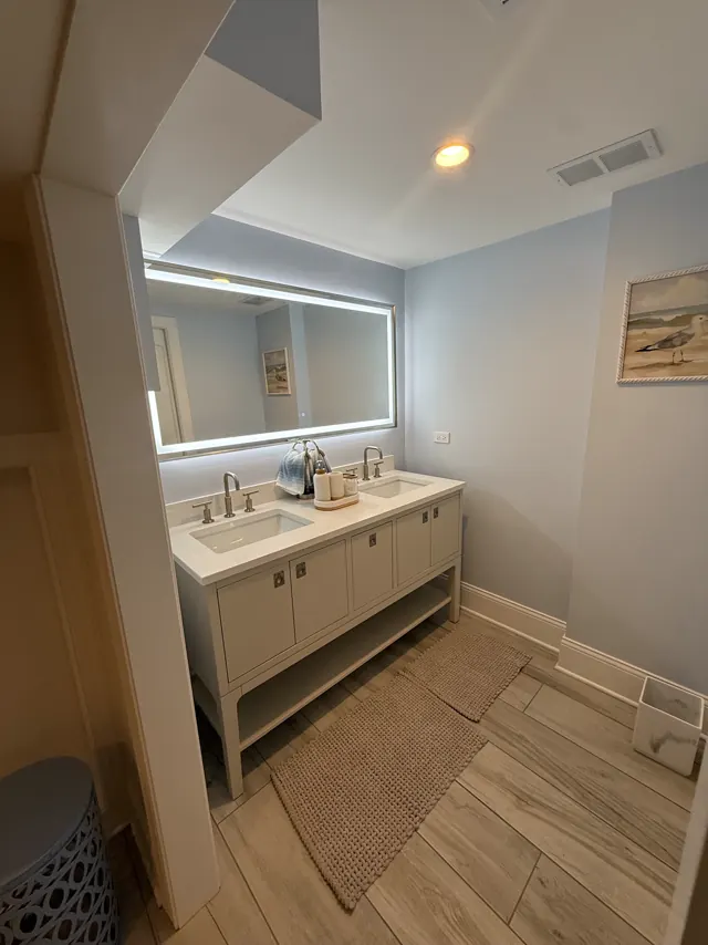 White double vanity with a backlit mirror and wood-look tile floor